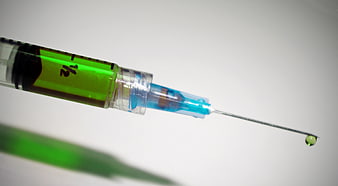 Close-up of syringe with green liquid and needle drop