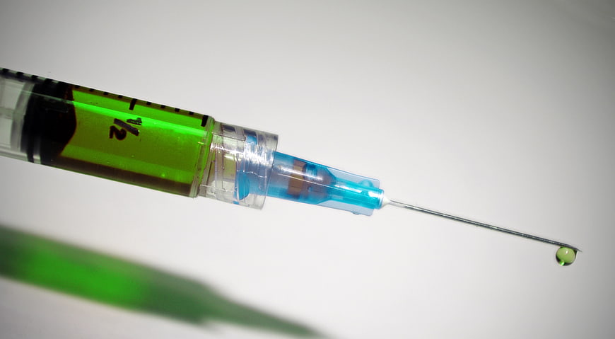 Close-up of syringe with green liquid and needle drop