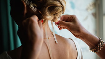 Close-up of hands tying a ribbon on a bride's updo hairstyle