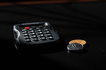 Black Calculator And Coins On Dark Surface