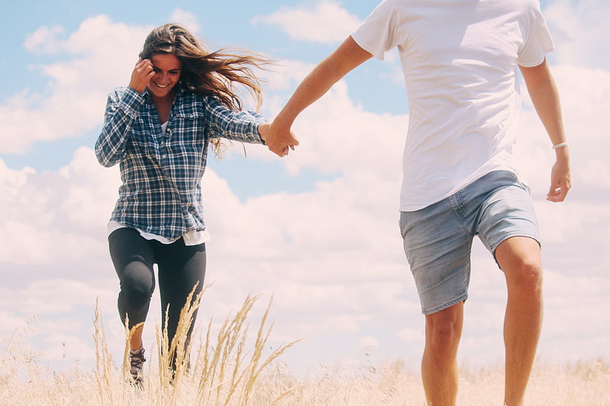 Happy couple holding hands running through a sunny field