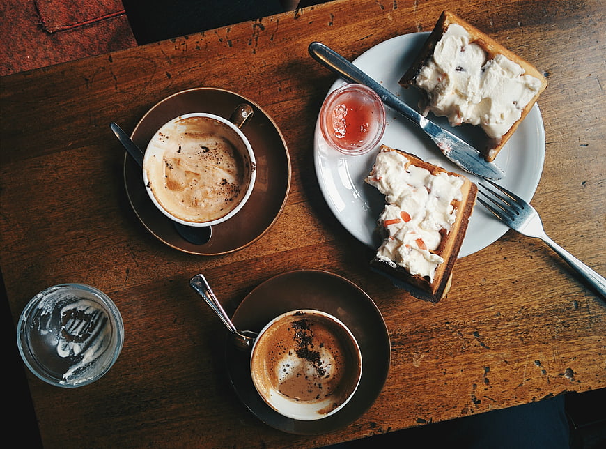 Overhead view of cappuccino and cream-topped waffles on rustic wood