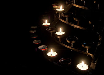 Five lit votive candles on a dark metal holder