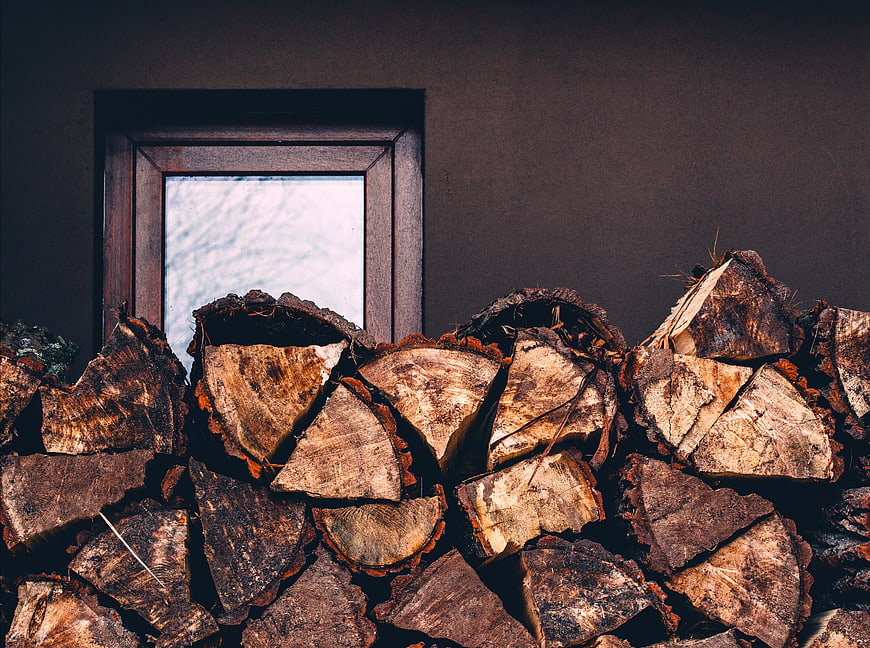 Stack of Firewood Against Dark Wall with Window
