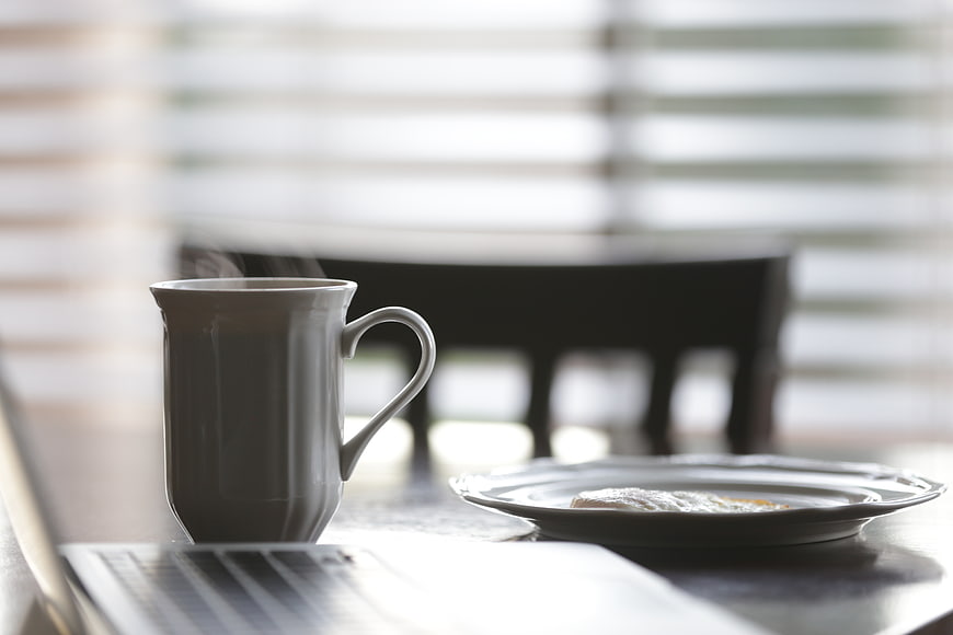 Steaming coffee mug and pastry on table with laptop