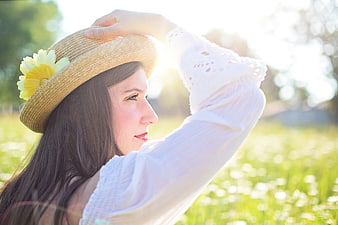 Young woman in straw hat with flower in sunny meadow