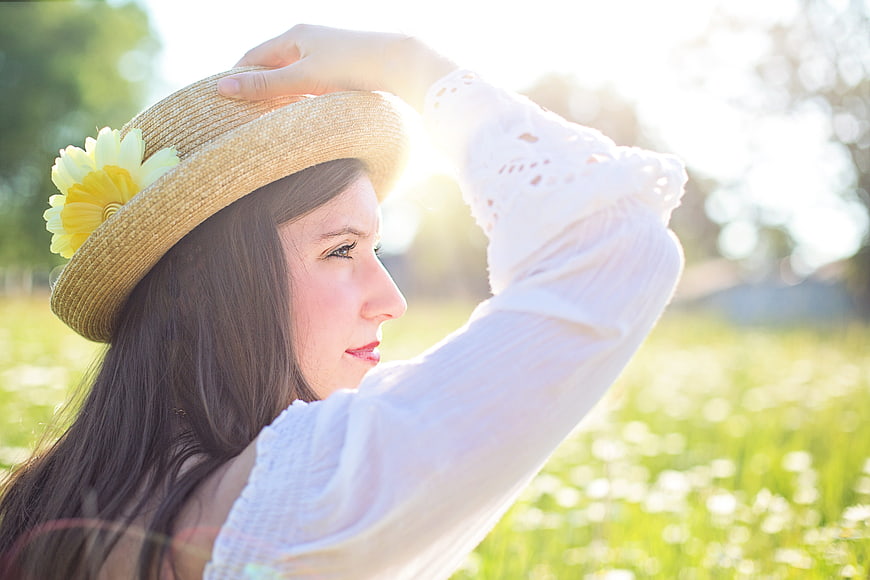 Young woman in straw hat with flower in sunny meadow