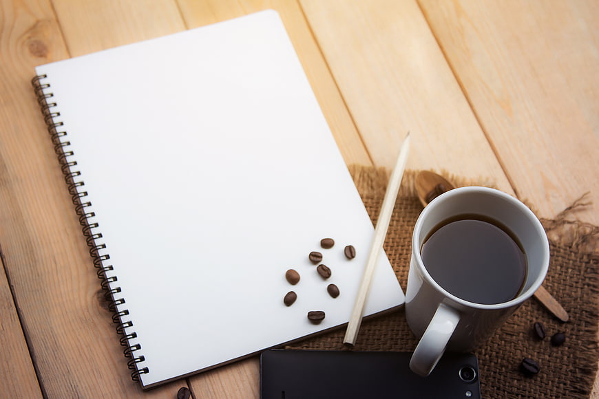 Flat lay of notebook, coffee, and smartphone on wooden desk