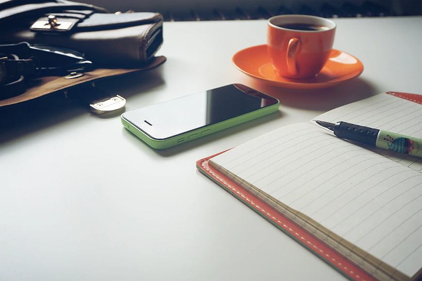 Green Smartphone, Coffee Cup, and Notebook on White Desk