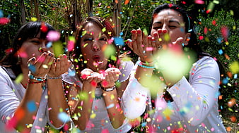 Three women blowing colorful confetti outdoors