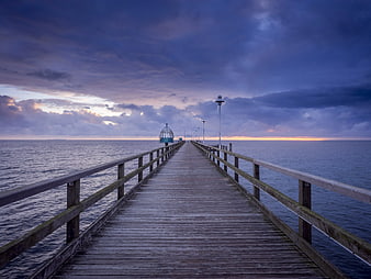 Wooden pier extending into ocean at twilight with dramatic clouds