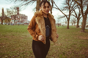 Confident woman in brown fur jacket standing in autumn park