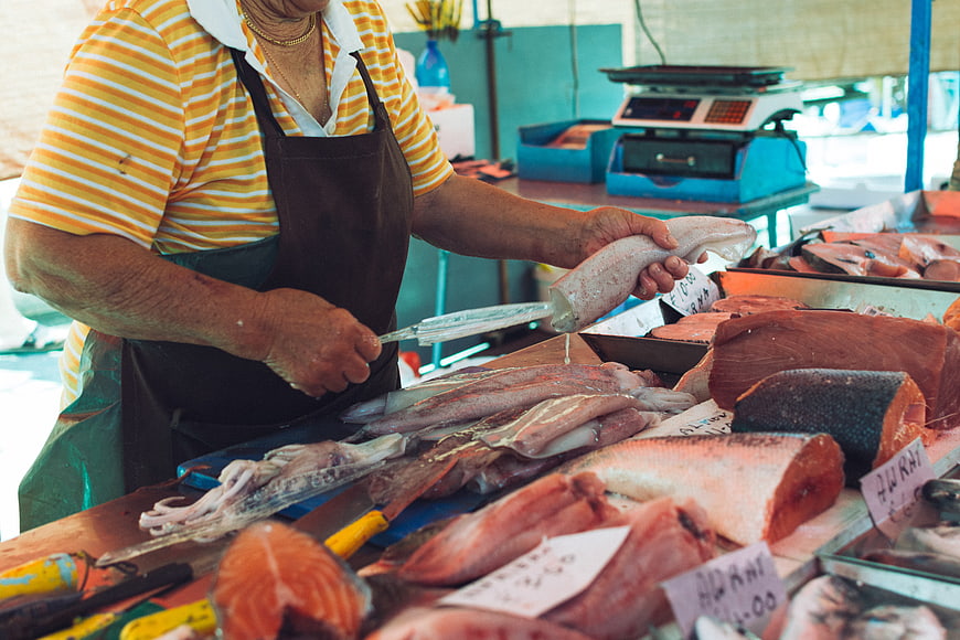 Fishmonger cutting fresh squid at outdoor seafood market stall