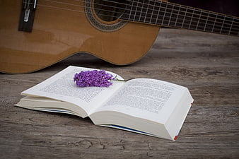 Open book with purple flowers and acoustic guitar on wood