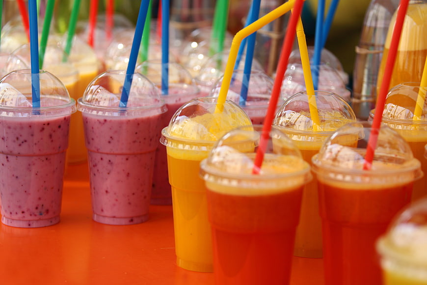 Colorful fruit smoothies with straws on orange table