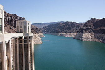 Huge concrete dam structure overlooking turquoise reservoir and canyon