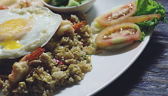 Close-up of shrimp fried rice with fried egg and tomato garnish