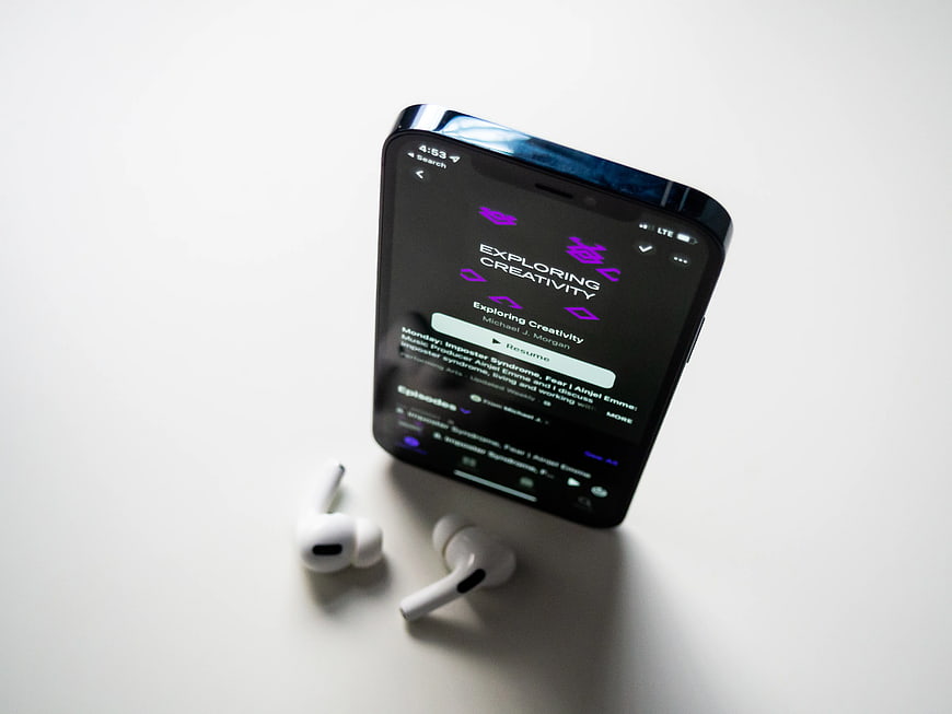 Smartphone Playing Podcast with Wireless Earbuds on White Surface