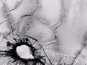 Black and white close-up of shattered glass with bullet hole