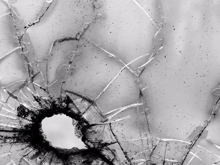 Black and white close-up of shattered glass with bullet hole