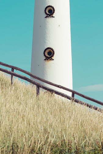 White Lighthouse Tower with Rusty Windows Against Blue Sky