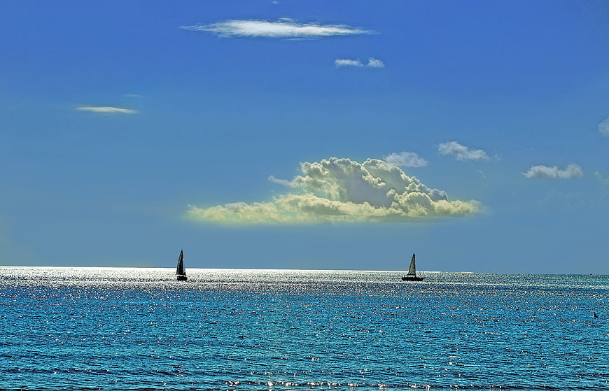 Sailboats on Sparkling Blue Ocean Under Cloudy Sky