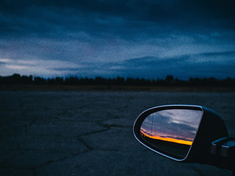 Car side mirror reflecting sunset on cracked pavement
