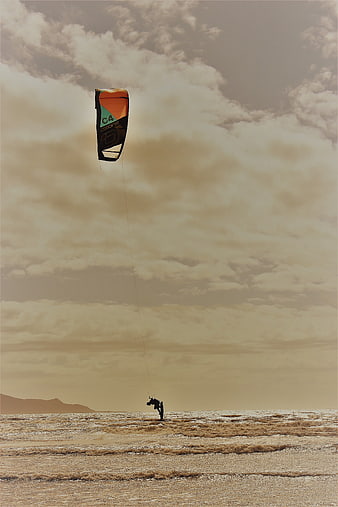 Kitesurfer riding waves under dramatic cloudy sky