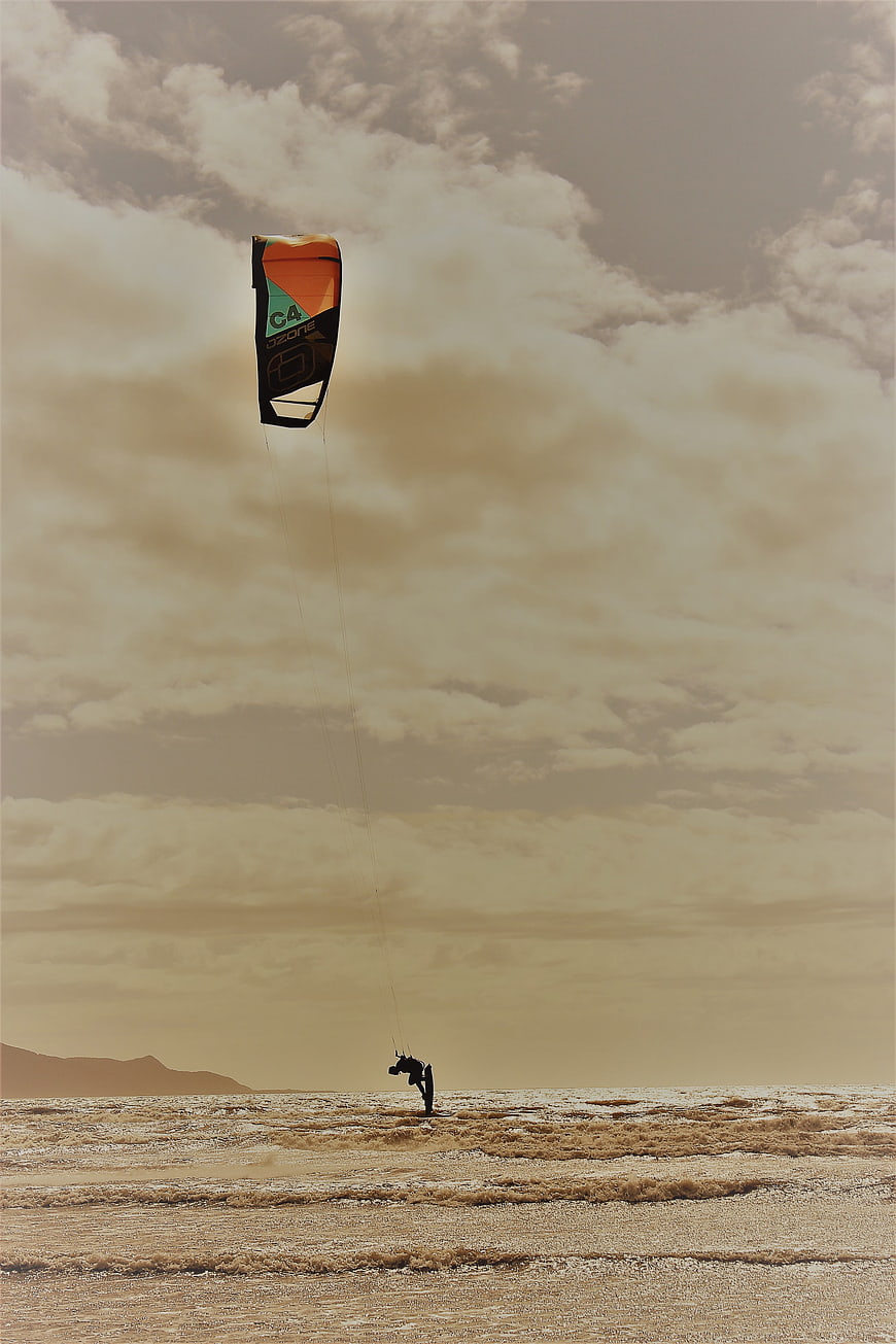Kitesurfer riding waves under dramatic cloudy sky