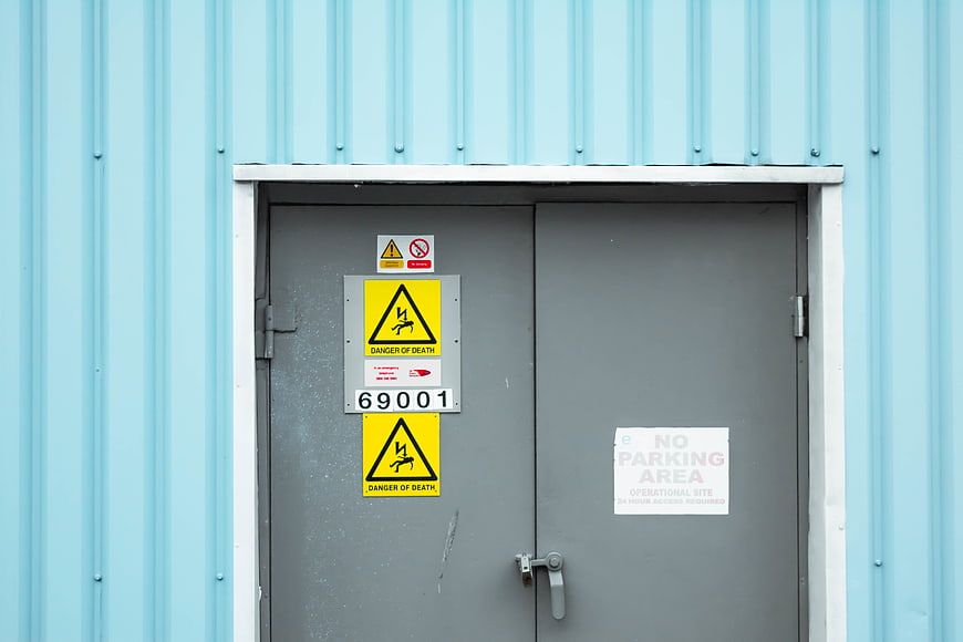Grey industrial double doors with danger of death warning signs