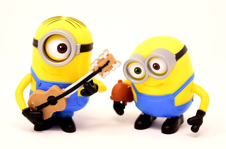 Two Minion Toy Figures Playing Guitar And Drums On White Background