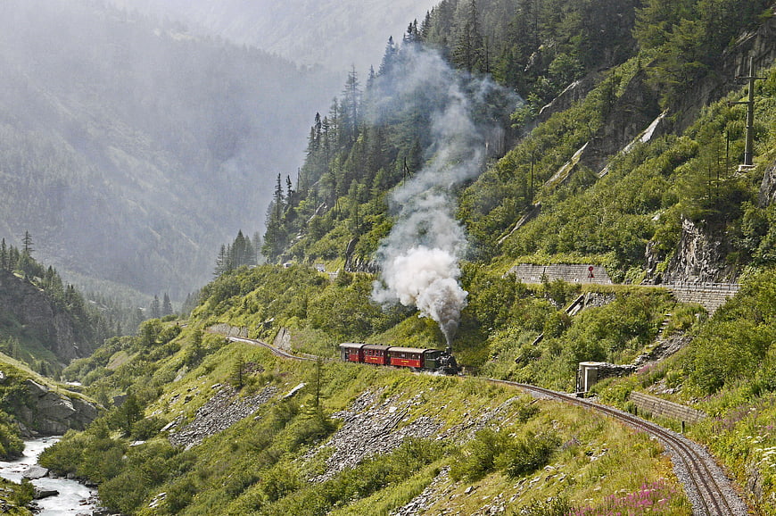 Vintage red steam train winding through lush green Swiss mountain valley