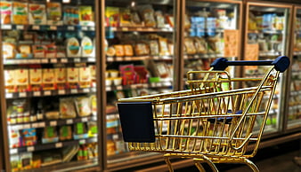 Miniature golden shopping cart in front of blurred supermarket shelves