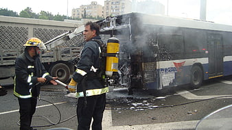 Firefighters extinguishing a burning bus on a city street