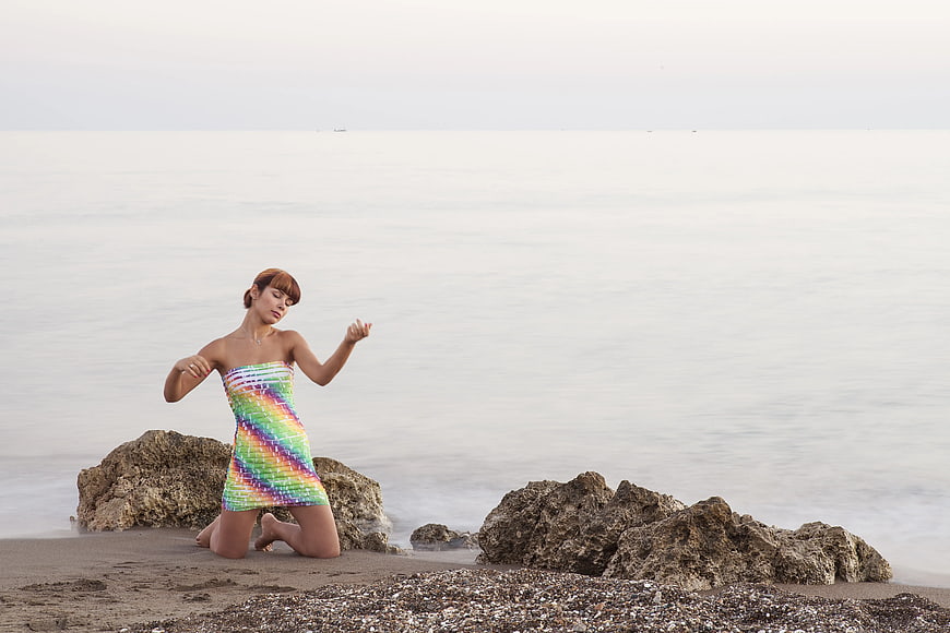 Woman in Rainbow Dress Kneeling on Beach
