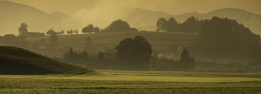 Misty golden morning landscape with rolling hills and farmhouses