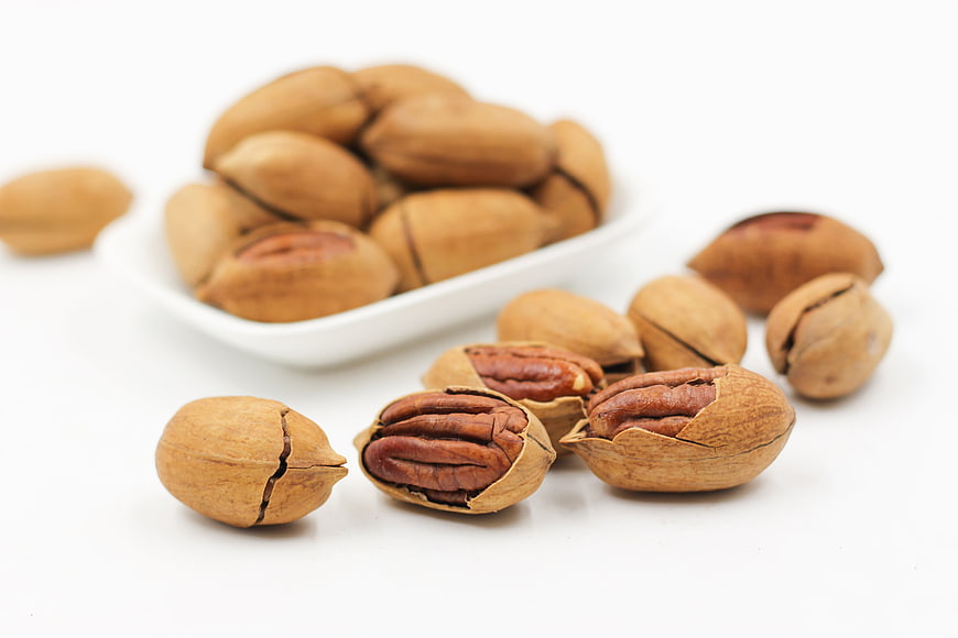 Cracked Pecan Nuts in White Bowl on White Background