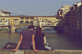 Couple sitting by river looking at historic bridge in Florence