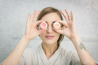 Woman holding lip balm tins over eyes playfully