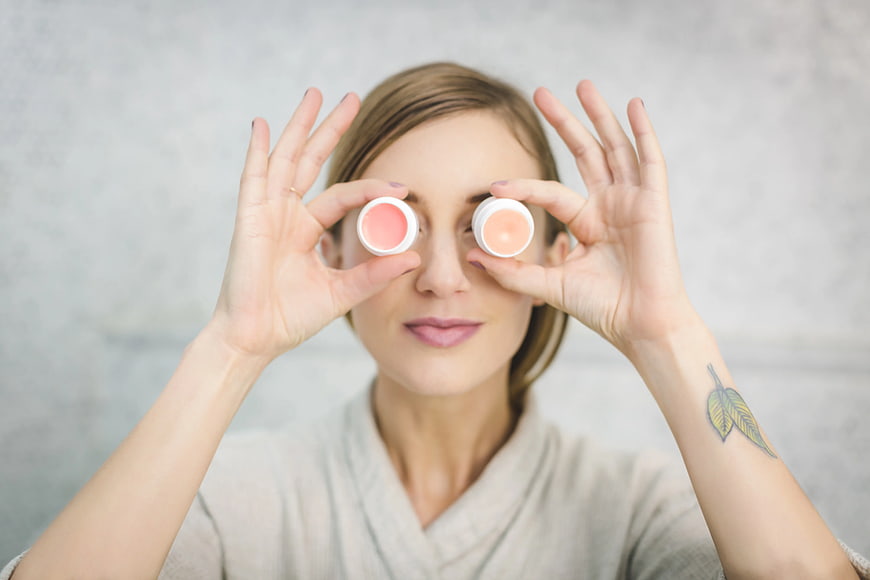 Woman holding lip balm tins over eyes playfully