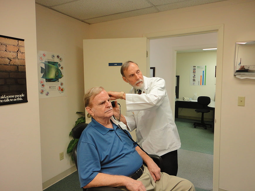 Senior male patient receiving hearing aid fitting from doctor in clinic