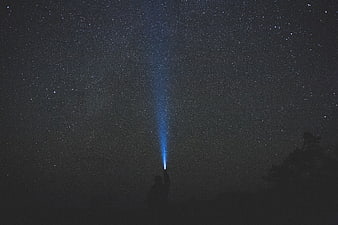 Silhouette of Person Holding Flashlight Beam into Starry Night Sky