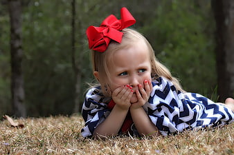 Cute little girl with red bow lying in grass