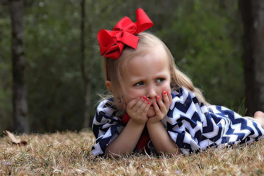 Cute little girl with red bow lying in grass