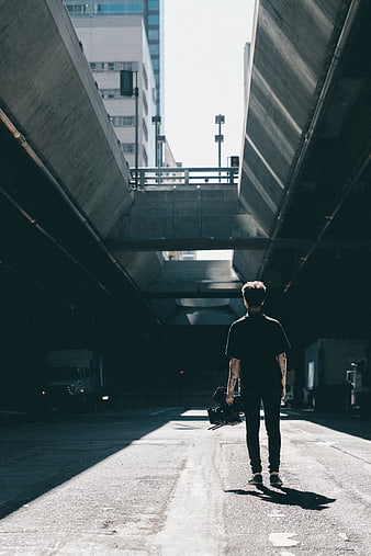 Man with Camera Walking Under Concrete Overpass