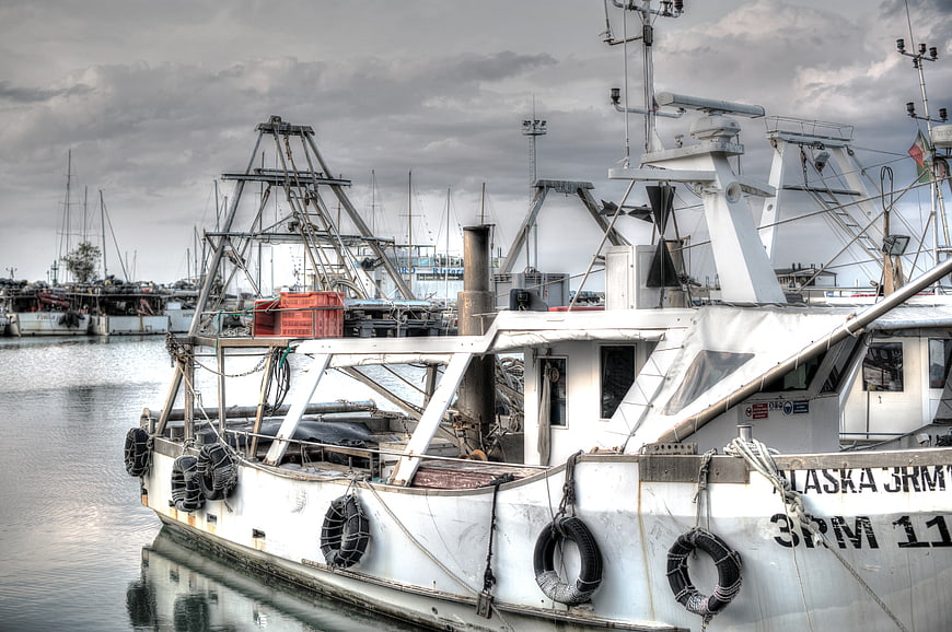 White fishing boat docked in harbor under cloudy sky