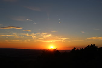 Golden sunset over silhouetted forest landscape with clouds