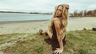 Blonde Woman in Black Dress Sitting on Beach with City Skyline