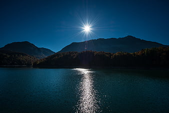 Sunburst over serene lake with mountain silhouette and water reflection