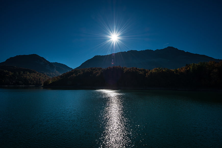 Sunburst over serene lake with mountain silhouette and water reflection